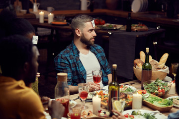 Portrait of bearded young man playing guessing game with friends during dinner party, copy space