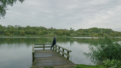 Obraz premium Autumn mood at the lake. Woman with warm clothes on a dock at a lake.Cloudy sky.