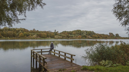 Naklejka premium Autumn mood at the lake. Woman with warm clothes on a dock at a lake.Cloudy sky.