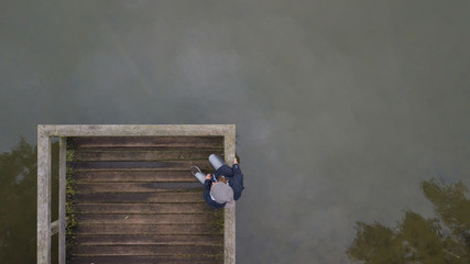 Autumn mood at the lake. Woman with warm clothes on a dock at a lake.Drone view.