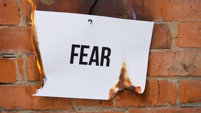 The inscription on a white A4 size sheet against the background of an orange brick wall. The paper with the black word Fear burns, smoke and turns into ashes. Business concept.
