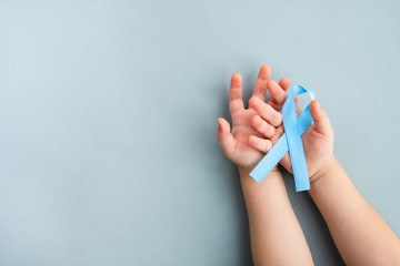 Child hands hold light blue Prostate cancer awareness ribbon on a light background. Medicine and...