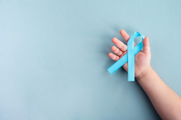Child hands hold light blue Prostate cancer awareness ribbon on a light background. Medicine and healthcare concept, Men's health. Copy space, top view