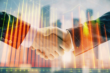 Double exposure of financial graph on cityscape background with two businessman handshake. Concept of stock market deal