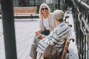 Pleased female sitting with her friend outdoors