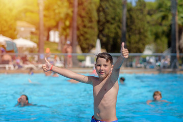 Portrait of Caucasian boy in swimming pool at resort. He is smiling, making like gestures and looking into camera.