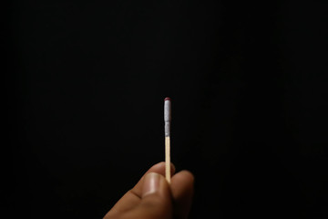 hand holding lit matchstick on black background
