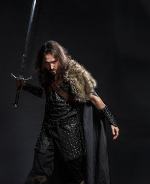 Man dressed in medieval armor and raincoat with longs word fighting against enemy. Courage fantasy warrior knight with long hair concept historical photo