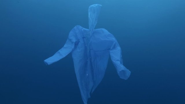 Blue plastic raincoat as a ghost slowly float in the blue water. Underwater plastic pollution of the Ocean. Plastic garbage environmental pollution problem. Slow motion, Movement forward. 