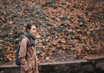 Autumn outdoor portrait of beautiful young woman walking in autumn park, wearing beige coat and warm knitted scarf.