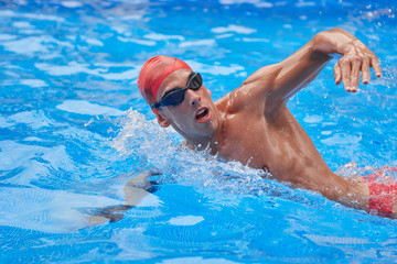 Swimmer in an outdoor pool, swimming in a crawl style, pulling his head out of the water to breathe, and with a raised arm, side view and top