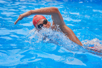 Swimmer in an outdoor pool, swimming in a crawl style, pulling his head out of the water to breathe, and with an arm raised above his head, side view and from above