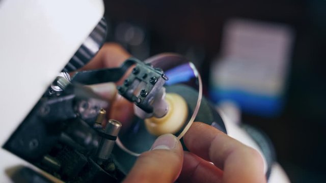 Manufacture of lenses for glasses. Close-up hands of optician making lense for eyeglasses on a modern equipment. Close-up.