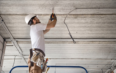 Electrician installer with a tool in his hands, working with cable on the construction site.