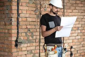 Builder handyman with construction tools, looking at the drawings on the construction site.