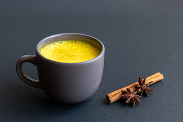 Golden (turmeric) milk in a gray cup on the dark background. Cinnamon and anise. 