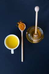 Golden (turmeric) milk in a white cup on the dark background. Jar with honey. A spoon with turmeric powder.  Top view.