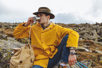 Fototapeta premium young stylish traveller enjoying drinking hor tea while sitting on the hill. close up photo