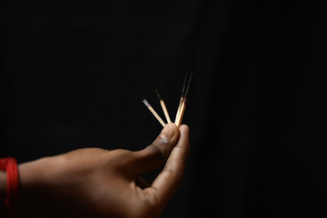 Hand holding an different extinguished matchstick on black background.