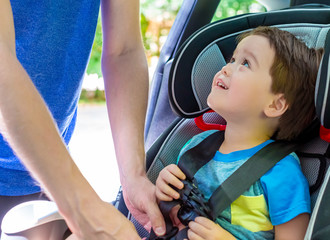 Toddler boy buckled into his car seat by his father