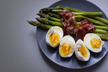 Healthy breakfast - green asparagus wrapped with bacon, boiled egg. Breakfast on a blue table closeup.