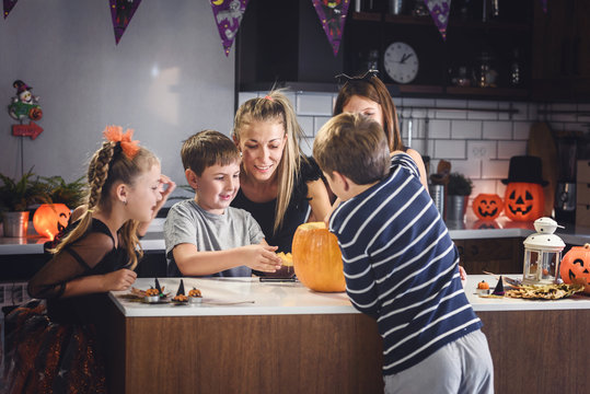 Mother carving Halloween pumpkin with children at decorated home kitchen