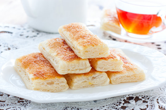 Baking tongues from puff pastry with sugar on a white plate, selective focus