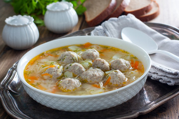 Homemade soup with meatballs and noodles in a white plate on a metal tray, selective focus