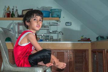 A boy wear red shirt sitting in the kitchen during waiting for a meal