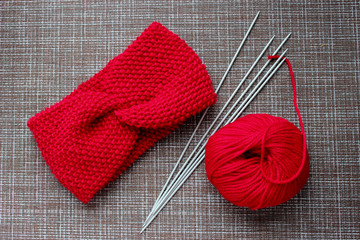 red knitted headband with knitting needles and ball of yarn