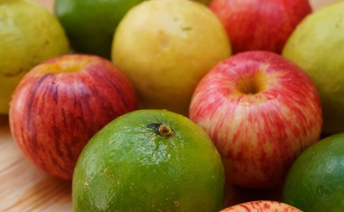 Limes, red apples and guavas on wood table background. Close up of a lime. Healthy food concept. Fresh fruits. 