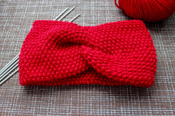 red knitted headband with knitting needles and ball of yarn