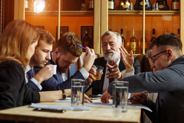 Full concentration at work. Group of young business people working and communicating while sitting at the office desk together with an old chief sitting in the head of a table