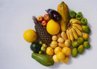 Fruits, starches and vegetables on white table background. Pineapple, apple, eggplant, mango, bananas, potatoes, bell pepper and tomatoes. 