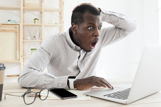 Frustrated Shocked African Man Having Problems, Feel Confused Looking At Laptop Screen At Office