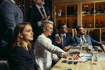 close up of pretty blonde businesswoman sitting close to brunette female partner at table enthusiastically looking at presentation of young coworker at business meeting