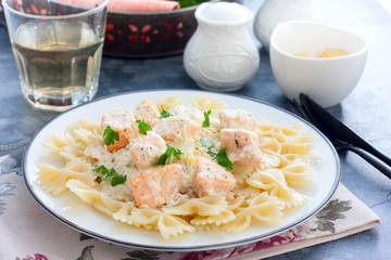 Farfalle with salmon in a creamy sauce and a white plate, horizontal