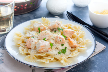 Farfalle with salmon in a creamy sauce and a white plate, horizontal
