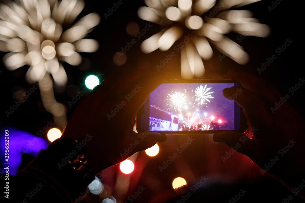 Wall mural Silhouette of hands with mobile cell phone to take a photo of fireworks.