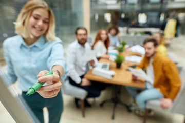 Close up of green marker in delicate hand of young charming woman against blurred background of...