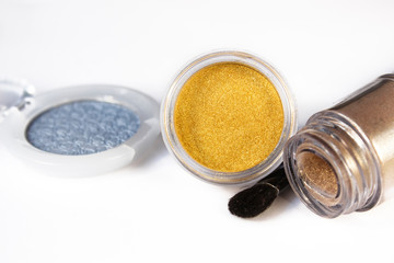 Gold, blue eye shadows, shimmer and eye brush  isolated on white background. Concept of makeup and beauty.