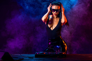 Young sexy woman dj playing music. Headphones and dj mixer on table. Colorful Smoke on background