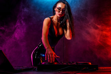Young sexy woman dj playing music. Headphones and dj mixer on table. Smoke on background