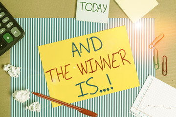 Word writing text And The Winner Is. Business photo showcasing announcing who got first place at competition or exam Striped paperboard notebook cardboard office study supplies chart paper