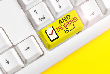 Text sign showing And The Winner Is. Business photo showcasing announcing who got first place at competition or exam White pc keyboard with empty note paper above white background key copy space