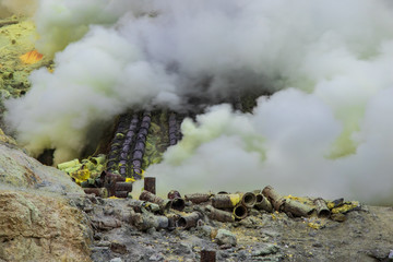 Sulfur mining operation in Mount Ijen Crater, East Java, Indonesia. Toxic gas escaping from volcanic vents. Pipes to divert the gas for condensing the sulfur for collection. 
