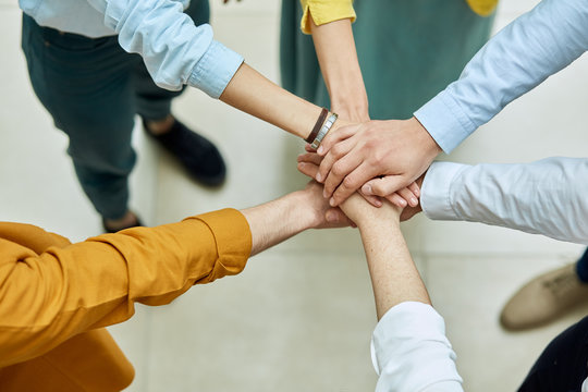 Friends keep hands together in sign of friendship and unity, shot from above, background of light coloured floor, people peace concept