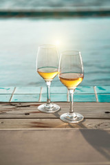 Two glasses of wine  on the edge of infinity swimming pool with panoramic views of the sea at sunset. Drink, celebrate, vacation and summer concept.