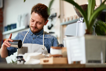 Handsome adult barista with stylish beard, makes ground coffee behind wooden counter, in modern cafe, shot from below