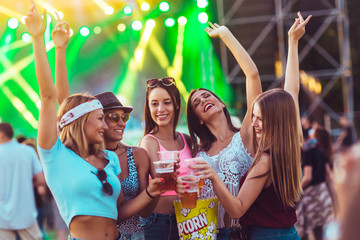Female friends dancing and toasting with beer at the music festival